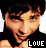 Pixelated image of a person with dark hair and light skin, wearing black clothing, showing two variations where the word 'LOVE' changes color from white to cyan.