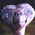 Pixelated static image of a light purple alien creature with large blue eyes and a small mouth, set against a dark background.