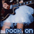 Animated icon shows a person in dark clothing holding a guitar, with light blue skirt and white shoes; text 'ROCK ON' appears at bottom.