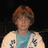 Pixelated image of a person with short brown hair wearing a light blue shirt under a white jacket with dark patterns against a black background.
