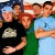 Pixelated static image of four people in close group pose with varied clothing colors and one person holding a small object.