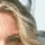 A woman with long wavy blonde hair smiles in a close-up portrait, her face partially cropped on the left side.