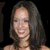 Pixelated portrait of a person with long dark hair smiling against black background, visible shoulders and neck.