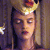 Pixelated image of a person with light skin tone, closed eyes, and red lips, wearing a golden crown-like headpiece against a dark background with blurred light patches.