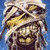 Mummy-wrapped figure with bandaged head and torso, golden eyes, smiling mouth on blue background.