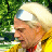 Pixelated static image of a person wearing a white cap and yellow clothing against green foliage background.