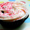A close-up of a cupcake with white frosting and red sprinkles, partially visible on a colorful background.