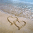 Beach scene with two heart shapes drawn in sand, one larger and one smaller overlapping; text 'dylan<333' appears above the hearts.