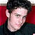 Pixelated close-up of a person with dark hair wearing a black top against a red background.
