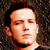 Static pixelated close-up of a person's face with dark hair and neutral expression against a dark background.