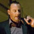 Static pixelated image of a person in formal attire holding a small object against a muted background.