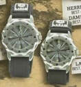 Two silver-toned wristwatches with black straps and circular dials, displayed on a textured brown surface.