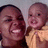 Two people in close proximity, one holding a child; both smiling with visible teeth against a light gray background.