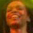 Pixelated static image of a person's face with warm orange and brown tones against a blurred green background, appearing as a low-resolution buddy icon.