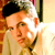 Pixelated static image of a person with dark hair wearing light-colored clothing, set against an indistinct background with warm tones and visible dithering artifacts.