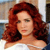 A pixelated close-up of a person with long, wavy red hair wearing a white top against a blurred background.