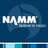 Pixelated blue background with white text 'NAMM' and a stylized globe graphic behind it, plus horizontal color bars at the bottom.