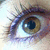 A pixelated close-up of a human eye with brown iris and blue highlights, showing eyelashes and surrounding skin tones.