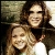 Two people with long brown hair smiling closely together in a pixelated static image.