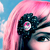A close-up of a person with bright pink hair wearing a black glittery flower-shaped hair accessory with a central pink-and-white skull design.