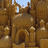 Pixelated sandcastle structure with arched entrance and towers under blue sky, surrounded by yellow pixel text.