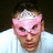 A person wearing a pink mask with white patterns, positioned next to cyan text on a black background.