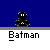Batman icon with yellow chest emblem and black cape, standing on gray platform against blue cityscape background with white buildings.