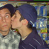 Two people in close proximity; one person kisses another on the cheek while wearing a dark blue beanie and dark blue striped shirt.