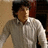Pixelated image of a person with brown hair wearing a light-colored collared shirt against a blurred background.