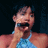 A pixelated contact sheet showing two frames of an animated icon featuring a person in a blue swimsuit holding a microphone against a dark background, with green text reading "Original Icons .com" on the right side.