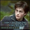 A character with round glasses and dark hair wears a dark jacket with white stripes, standing against a blurred green background while text reads "I DON'T GO LOOKING FOR TROUBLE..." below.