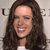 A pixelated close-up of a person with long dark brown hair, light skin, and a white top, set against a light gray background with partial text.