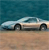 Pixelated image of a light-colored sedan on a sandy beach with a teal ocean background, viewed from the side.