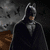 Batman in dark cowl and cape stands against gray stone background; purple-robed figure with sword appears on right side.