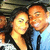 Two people in close proximity with one person's arm around the other, set against a blurred background.