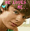 Pixelated image of a person with brown hair and red lips, showing text above the head that changes between 'HE LOVES HE.' and 'HE JUST DOESN'T KNOW IT.', accompanied by small heart symbols.