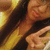 A person with long dark hair and a yellow top makes a peace sign, smiling in warm lighting.