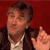 Pixelated image of a person with short dark hair wearing a dark jacket over a light shirt, set against a solid red background.