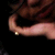 Pixelated close-up of a person's arm and hand with a small light-colored object near the wrist against dark background.