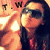 A person with long dark hair and sunglasses poses against a warm-toned background with repeated 'T.W' text, wearing a red patterned top.