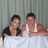 Two people under a white sheet with one person in black shirt and another in white tank top, showing time display change.