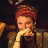 Pixelated static image of a person with red hair and light skin resting their chin on one hand, wearing dark clothing against a dark background.