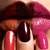 Close-up of a person's lips and fingers with dark brown, red, and pink nail polish on short nails against light skin.