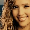 A close-up of a person with long, wavy light brown hair, smiling with visible teeth, against a blurred background.