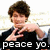 Pixelated image of a person with brown hair wearing a black shirt, making a hand gesture while text below reads "peace yo.".