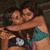 Two people in a close embrace, one wearing a blue polka-dot bikini top, with a small white object held between them.