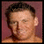 A static image of a person with short dark hair against a reddish background, wearing no shirt.