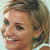 Pixelated close-up of a smiling person with light brown hair, visible ear, and teal earrings against a light background.
