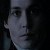 Pixelated grayscale portrait of a person with dark hair and a neutral expression, cropped to show upper face and neck against a dark background.