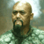 Pixelated image of a bald man with a dark beard wearing a green shirt against a blurred background.